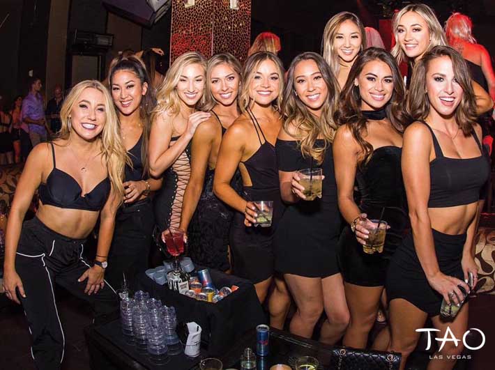 Ladies dressed in black dresses holding drinks at a TAO bottle service dance floor table